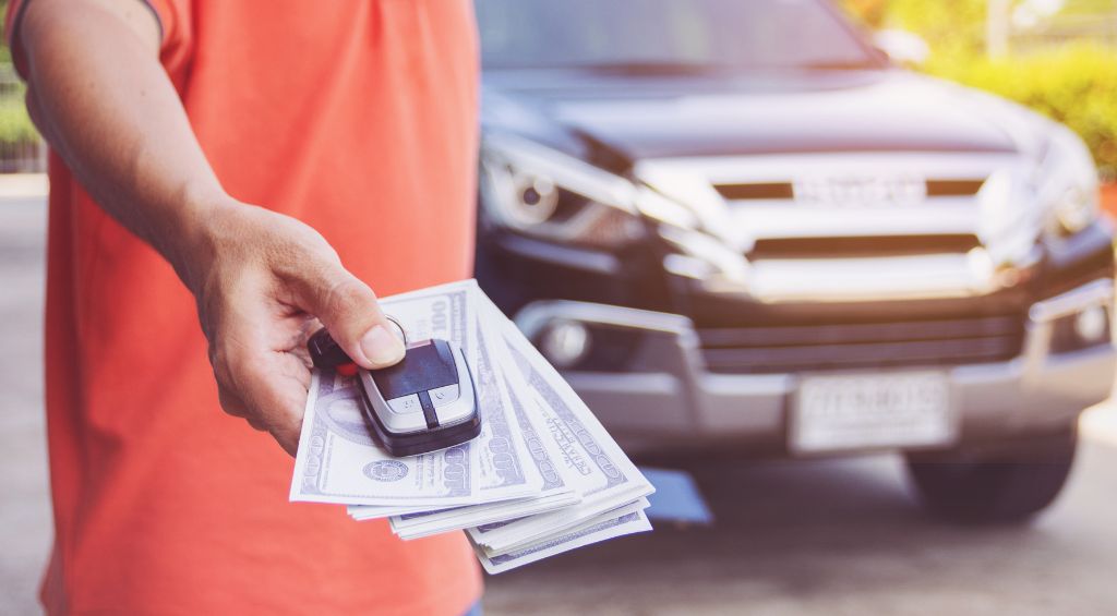  financiamento de veículos: pessoa segurando chave de carro com o carro atrás.